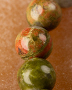 Detalle cercano de una cuenta de Jaspe Unakita con vetas naranjas y verdes