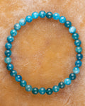 Pulsera de Apatita Azul de 6 mm, pieza completa en círculo sobre superficie de piedra ocre anaranjada