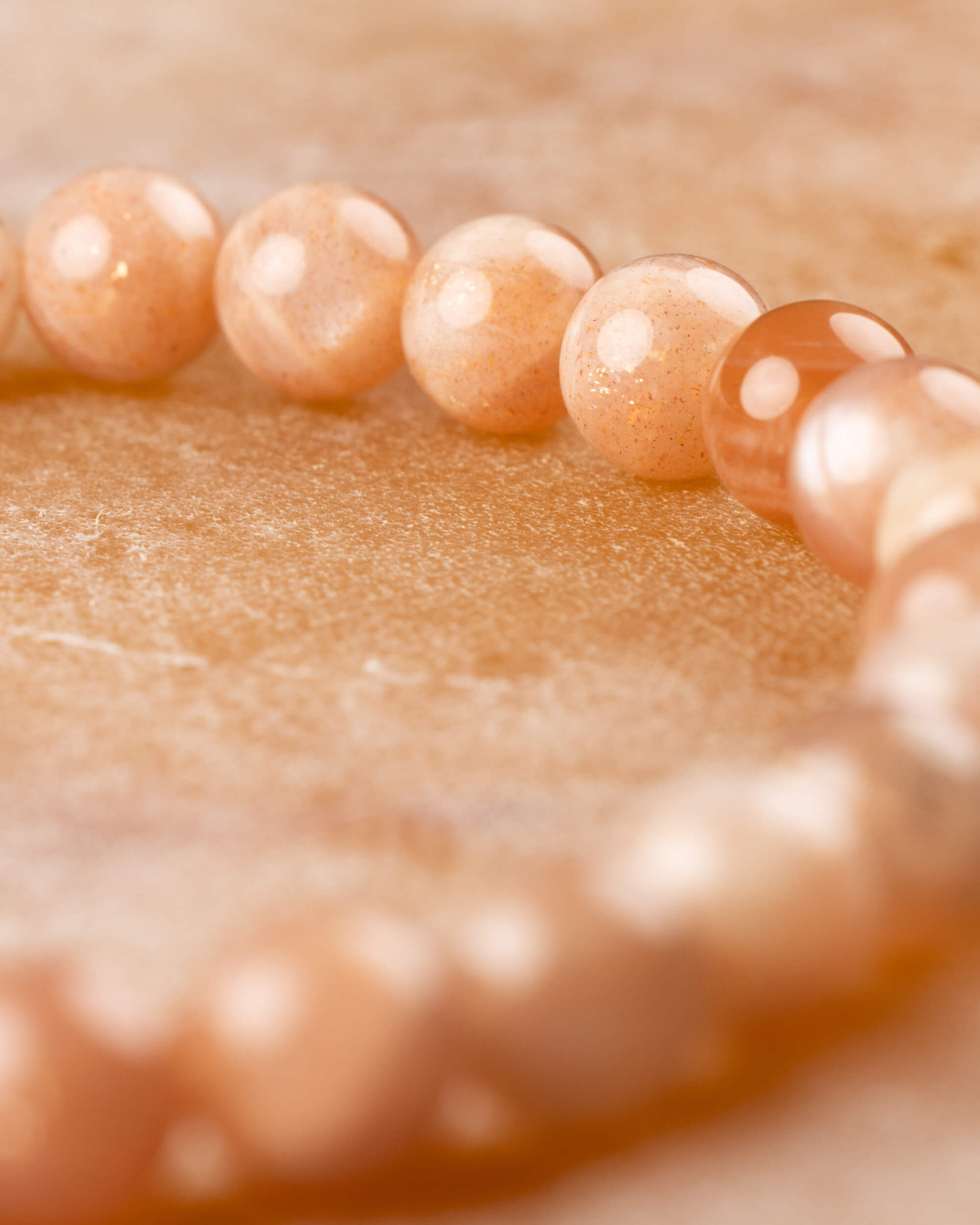 Pulsera de Piedra Sol Naranja en curva, con cuentas desenfocadas al fondo