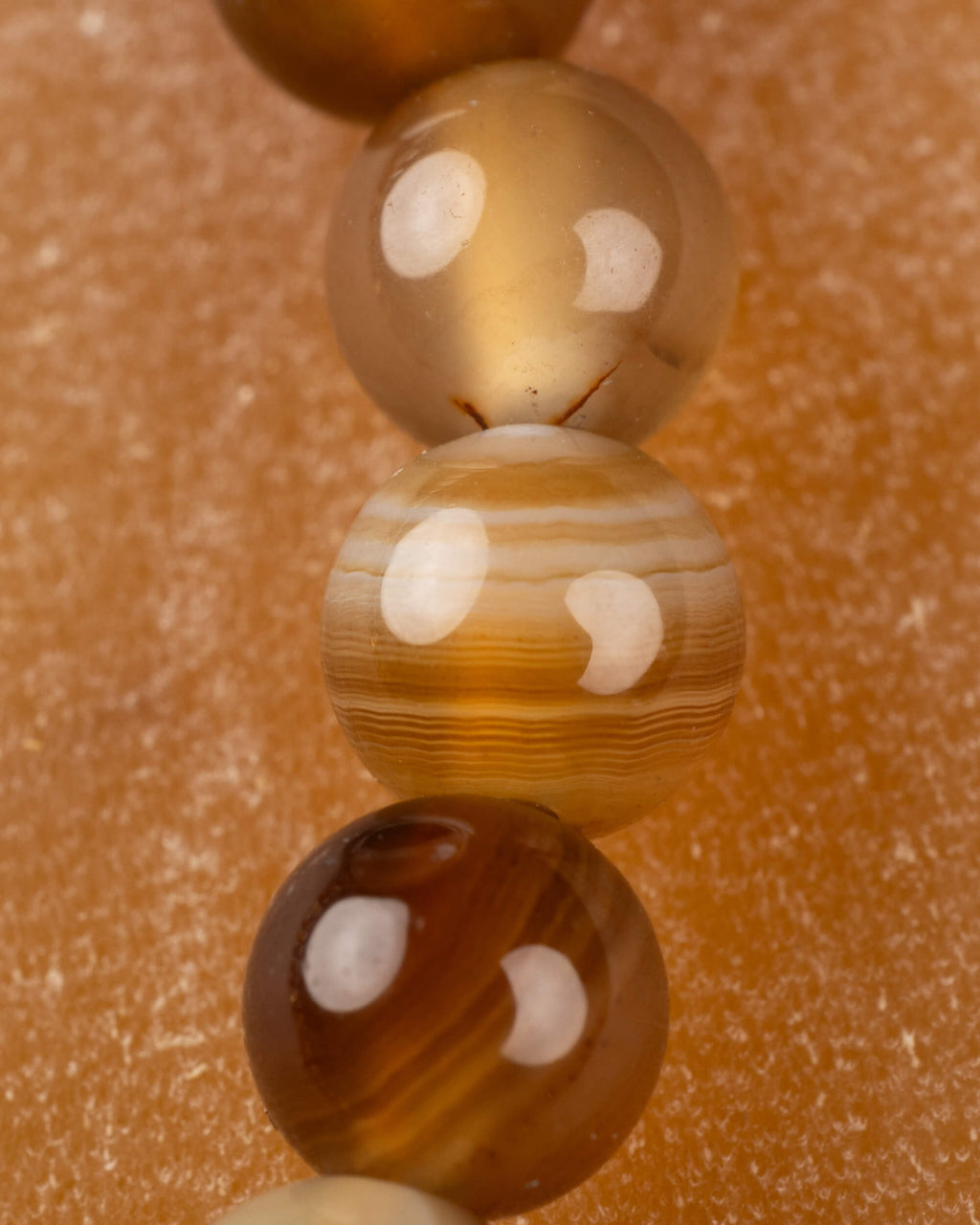 Detalle macro de cuentas doradas y rayadas de Ágata Café en fila vertical