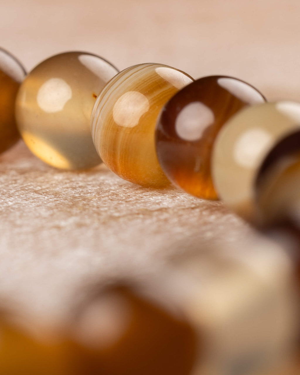 Detalle macro de cuentas doradas y rayadas de Ágata Café en la curva de la pulsera