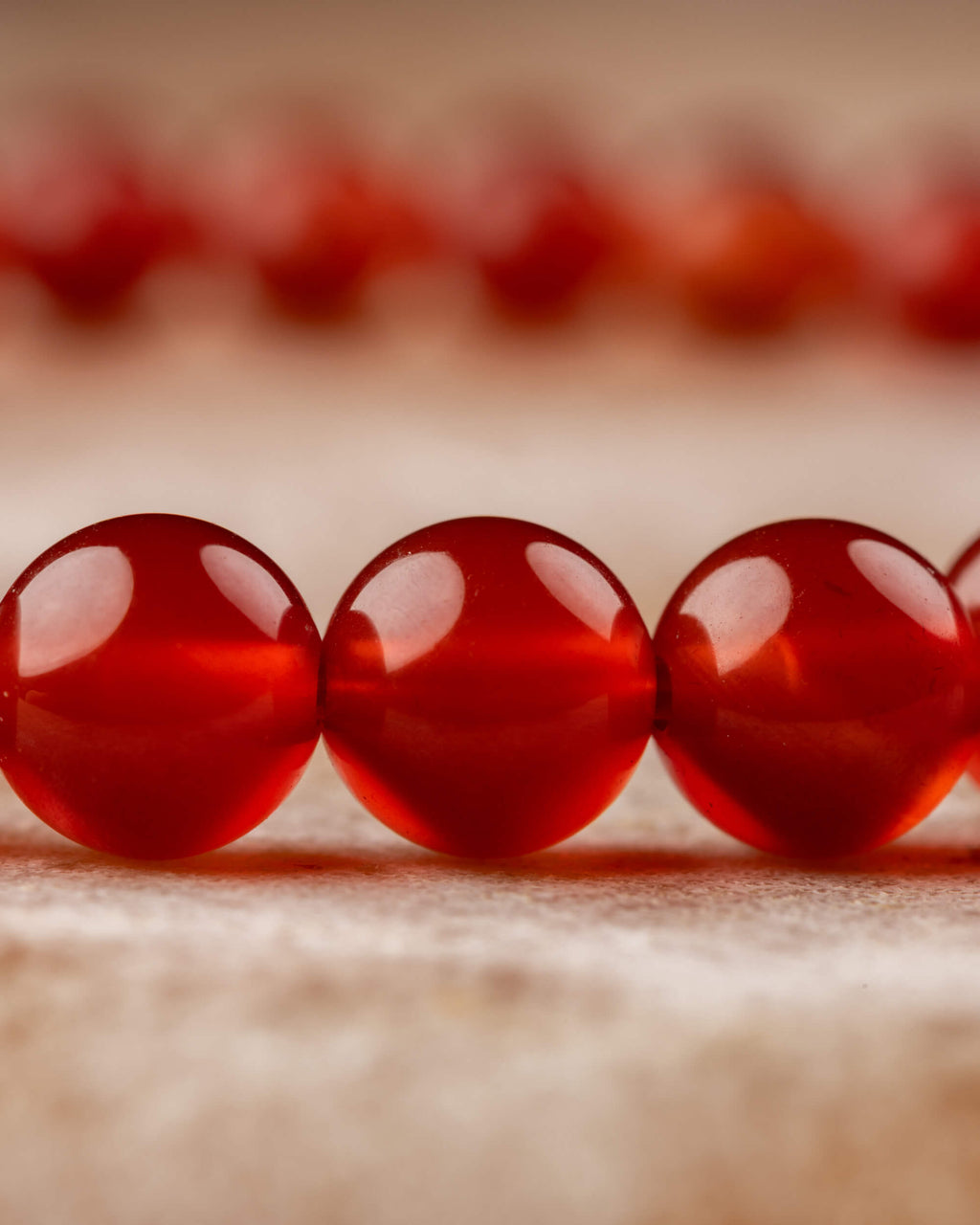 Vista en ángulo de las cuentas rojas de la pulsera de Cornalina sobre tela clara