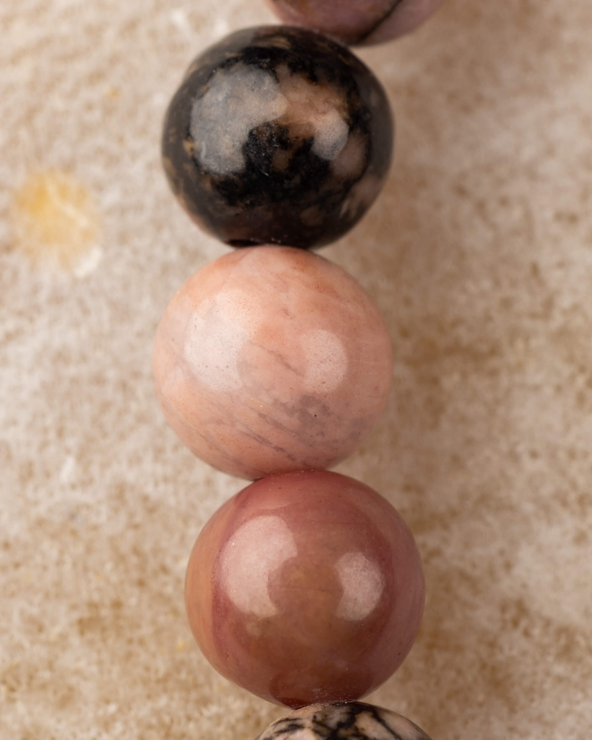Macro vertical de tres cuentas de Rodonita encaje negro, tonos rosa y café con vetas negras