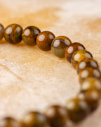 Pulsera de Pietersita amarilla en curva, cuentas doradas y cafés sobre superficie clara