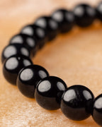 Pulsera de Turmalina Negra en curva sobre madera clara, enfoque frontal