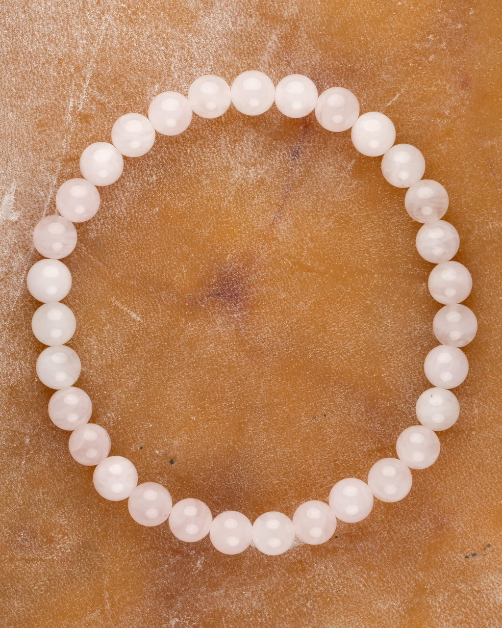 Pulsera de Cuarzo Rosa de 6 mm, pieza completa en círculo sobre superficie de piedra clara