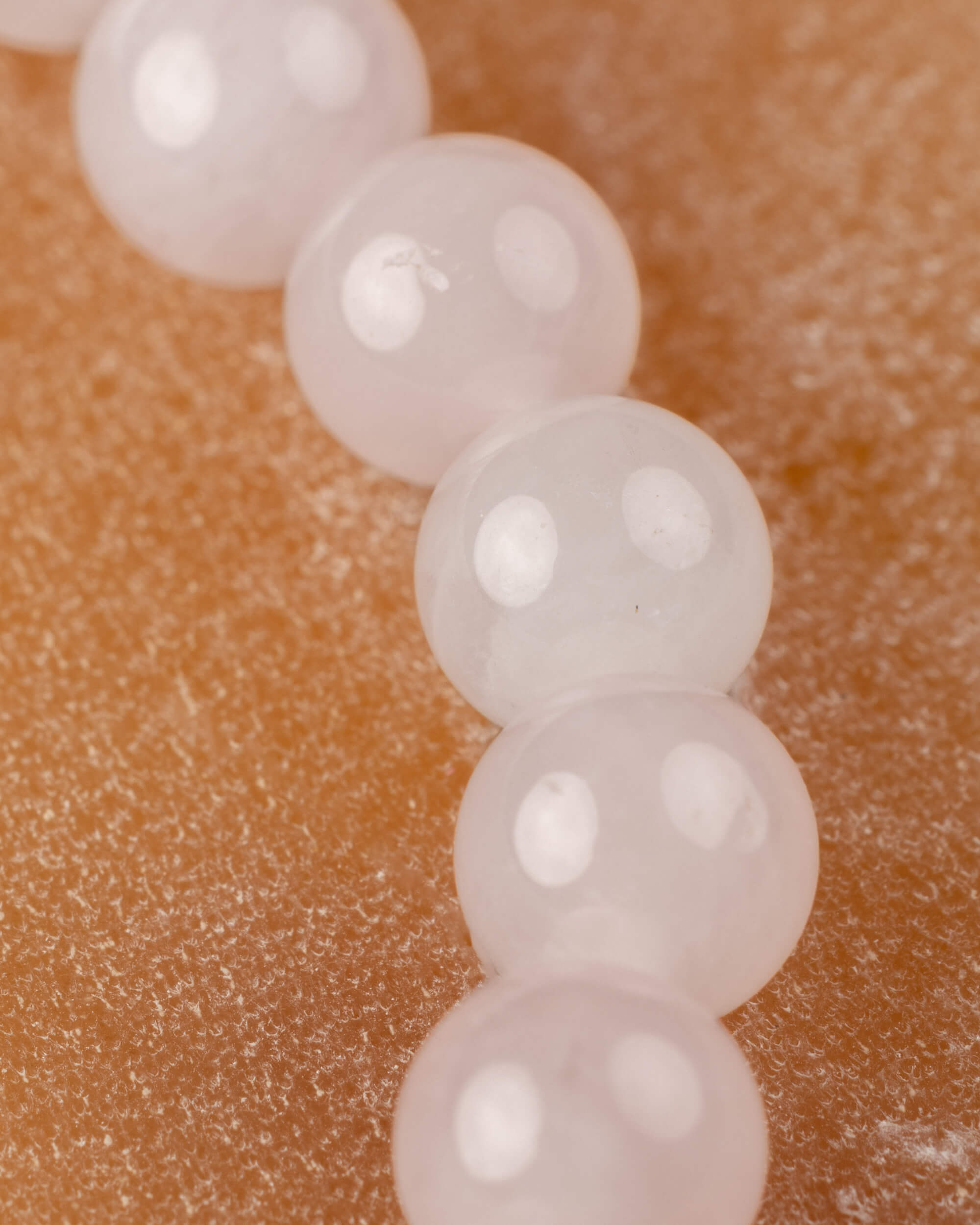 Detalle macro de las cuentas de Cuarzo Rosa en fila, veta blanca visible