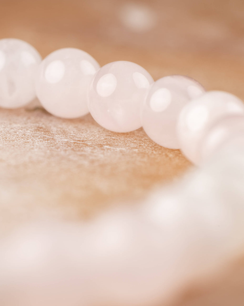 Detalle macro de las cuentas de Cuarzo Rosa, curva de la pulsera al fondo
