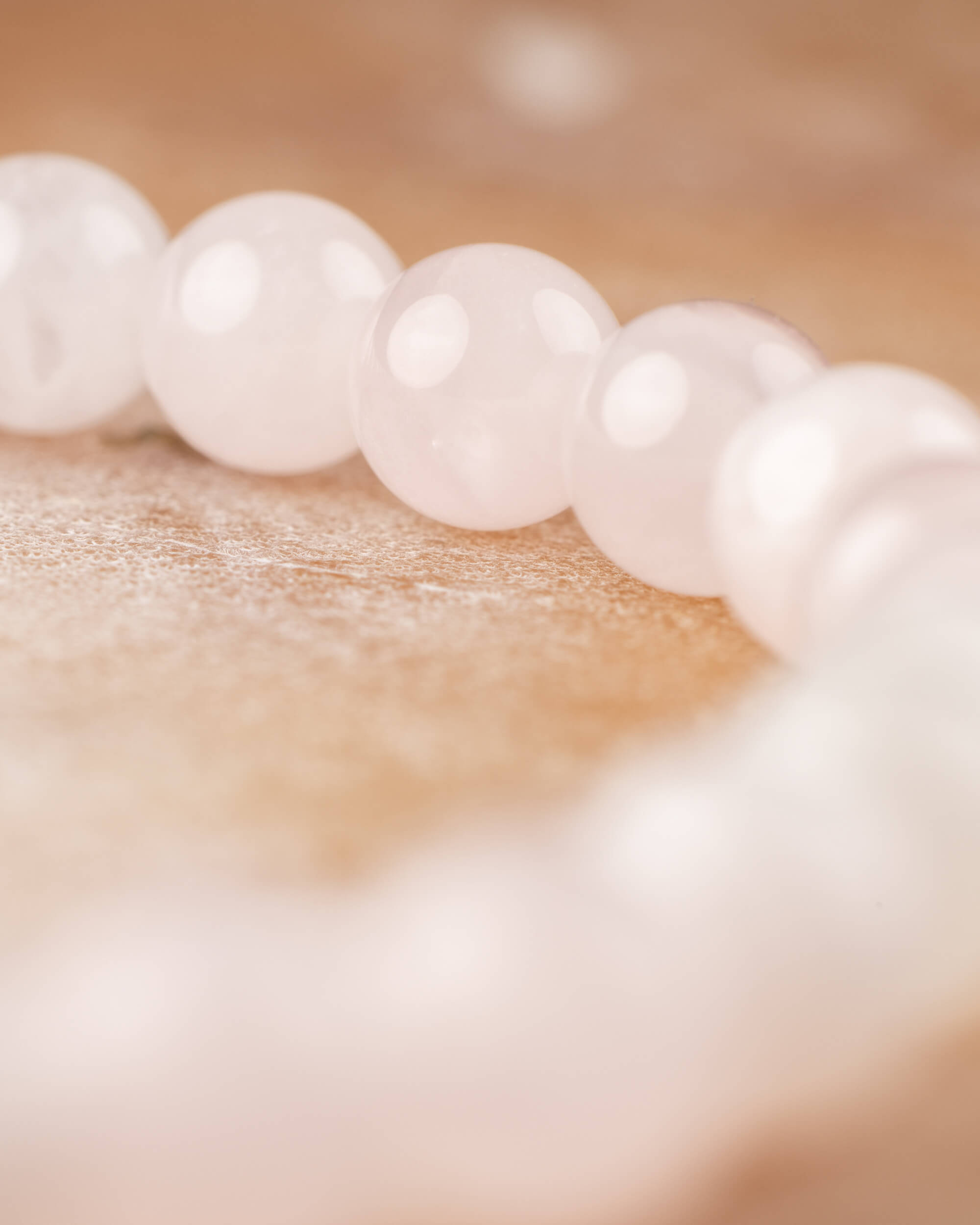 Detalle macro de las cuentas de Cuarzo Rosa, curva de la pulsera al fondo