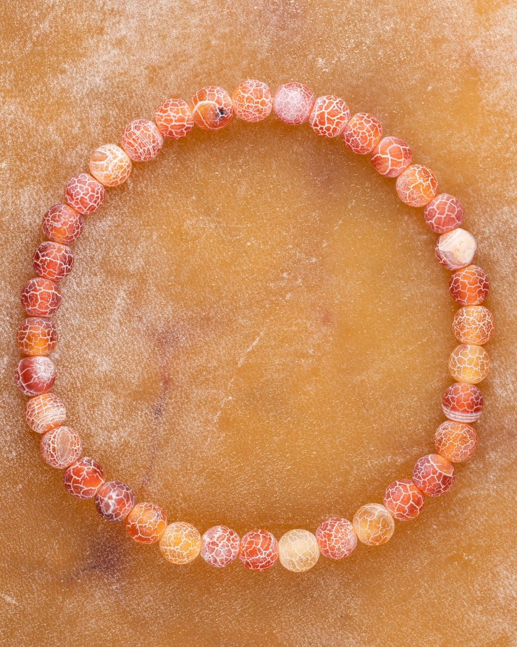 Pulsera de Ágata Craquelada de 6 mm en tonos naranja y rojo, pieza completa en circulo sobre superficie ocre