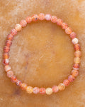 Pulsera de Ágata Craquelada de 6 mm en tonos naranja y rojo, pieza completa en circulo sobre superficie ocre