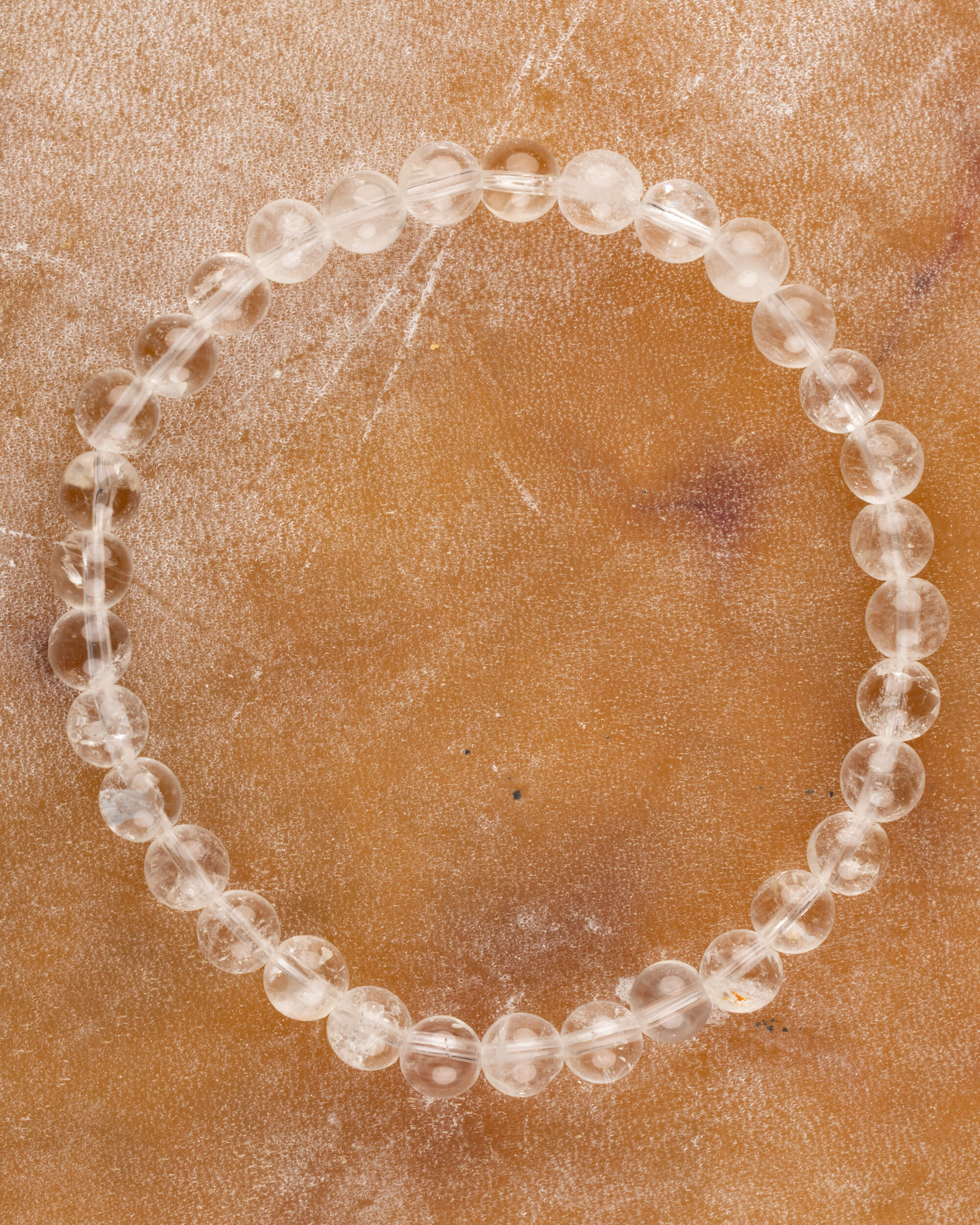 Pulsera de Cuarzo Transparente, pieza completa en círculo sobre superficie ambar