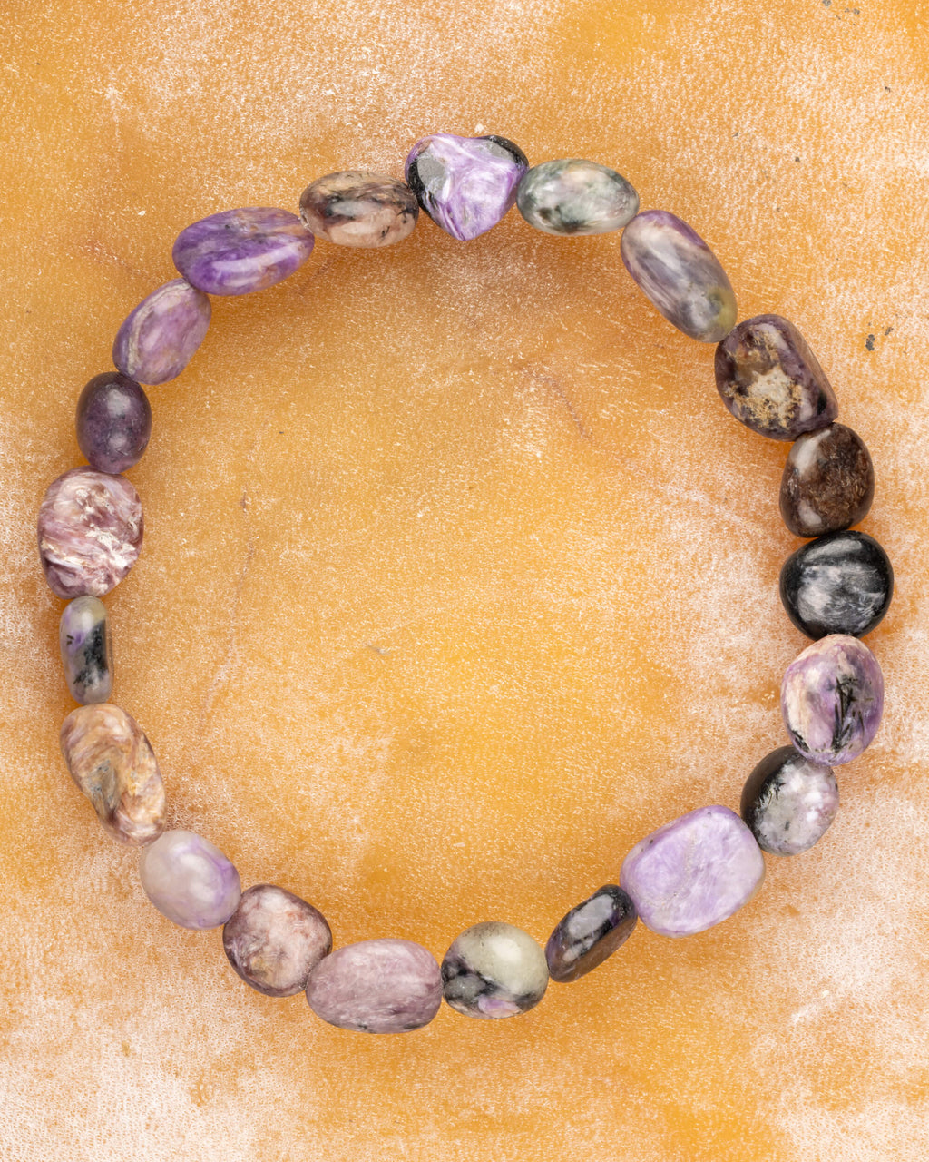 Pulsera de Charoita irregular, pieza completa en círculo sobre superficie color mostaza