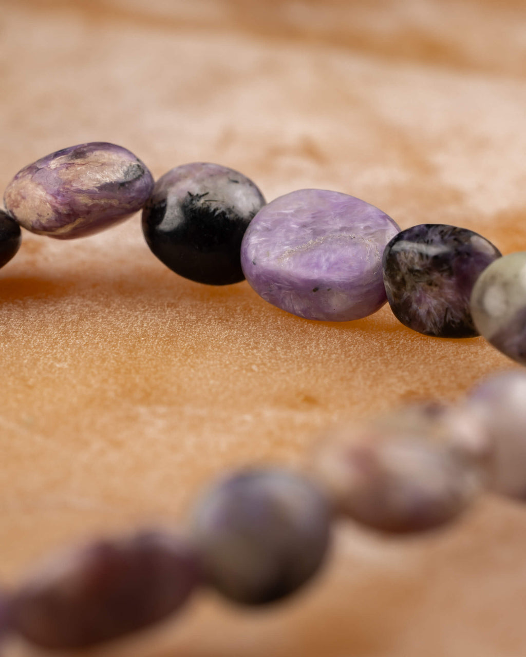 Pulsera de Charoita irregular en curva, piedras moradas y negras sobre madera clara