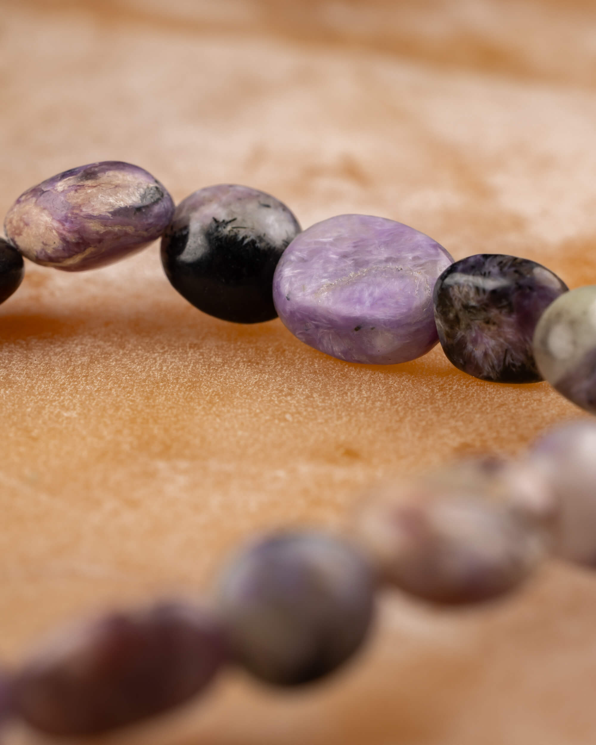 Pulsera de Charoita irregular en curva, piedras moradas y negras sobre madera clara