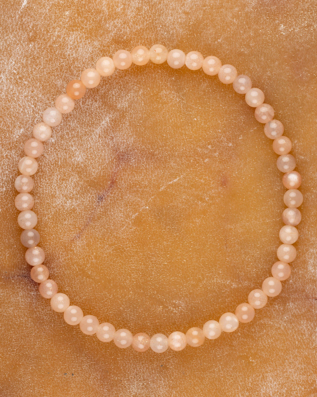 Pulsera de Piedra Sol Naranja de 4 mm, pieza completa en círculo sobre superficie dorada