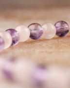 Pulsera de Amatista y Cuarzo Rosa en curva, cuentas vistas desde otro angulo sobre madera