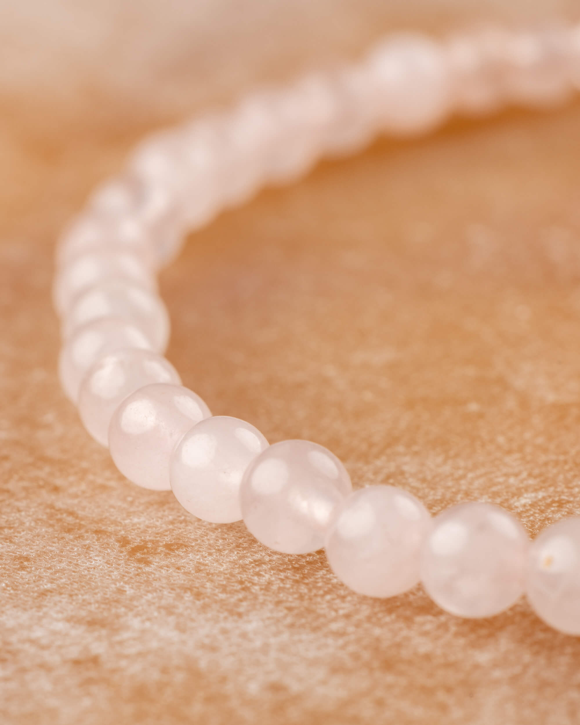 Pulsera de Cuarzo Rosa en curva, cuentas visibles desde otro angulo sobre superficie clara