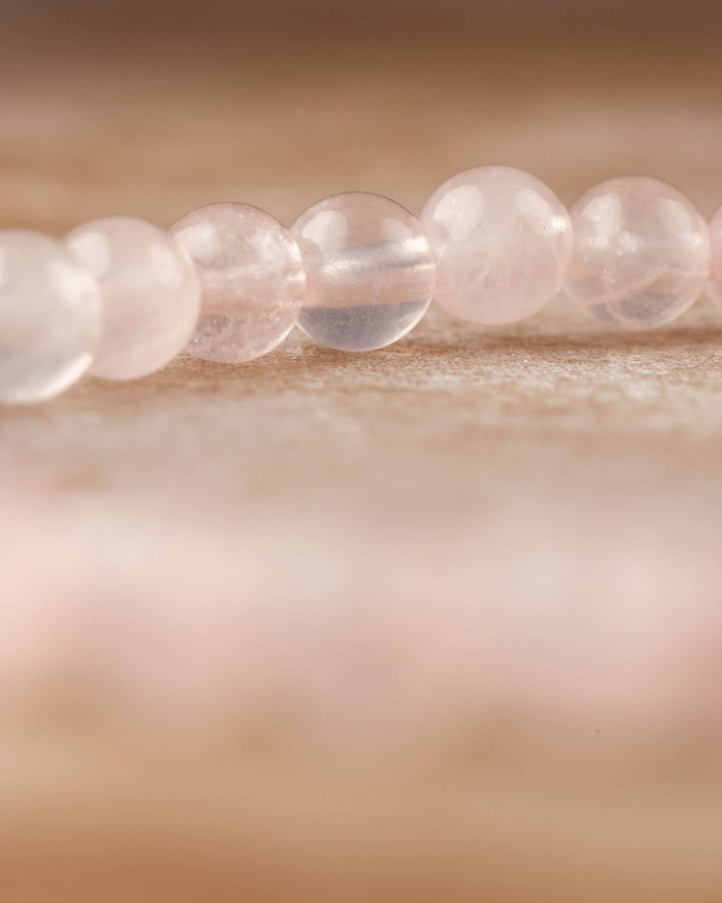 Pulsera de Cuarzo Rosa vista de perfil, cuentas en hilera sobre madera clara