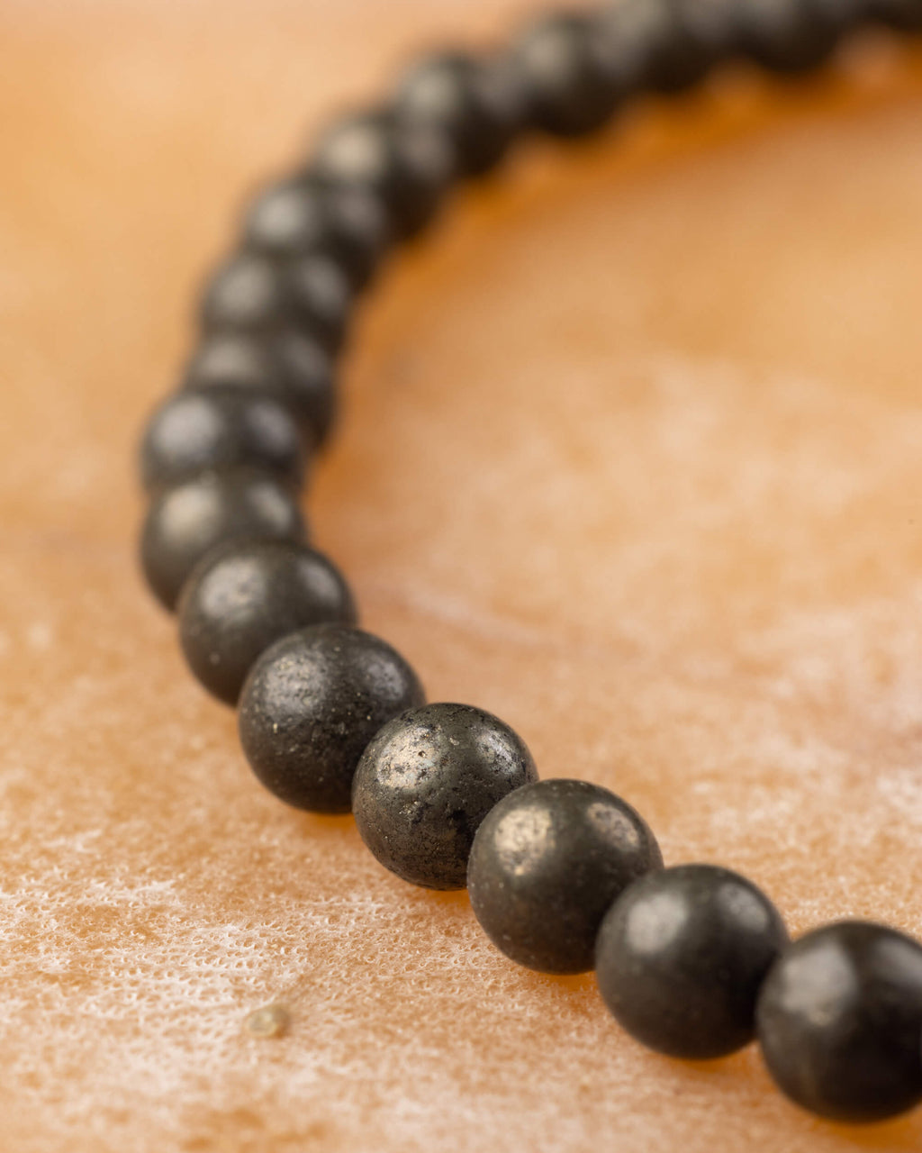 Pulsera de Pirita en curva, cuentas oscuras con brillo metálico sobre superficie clara