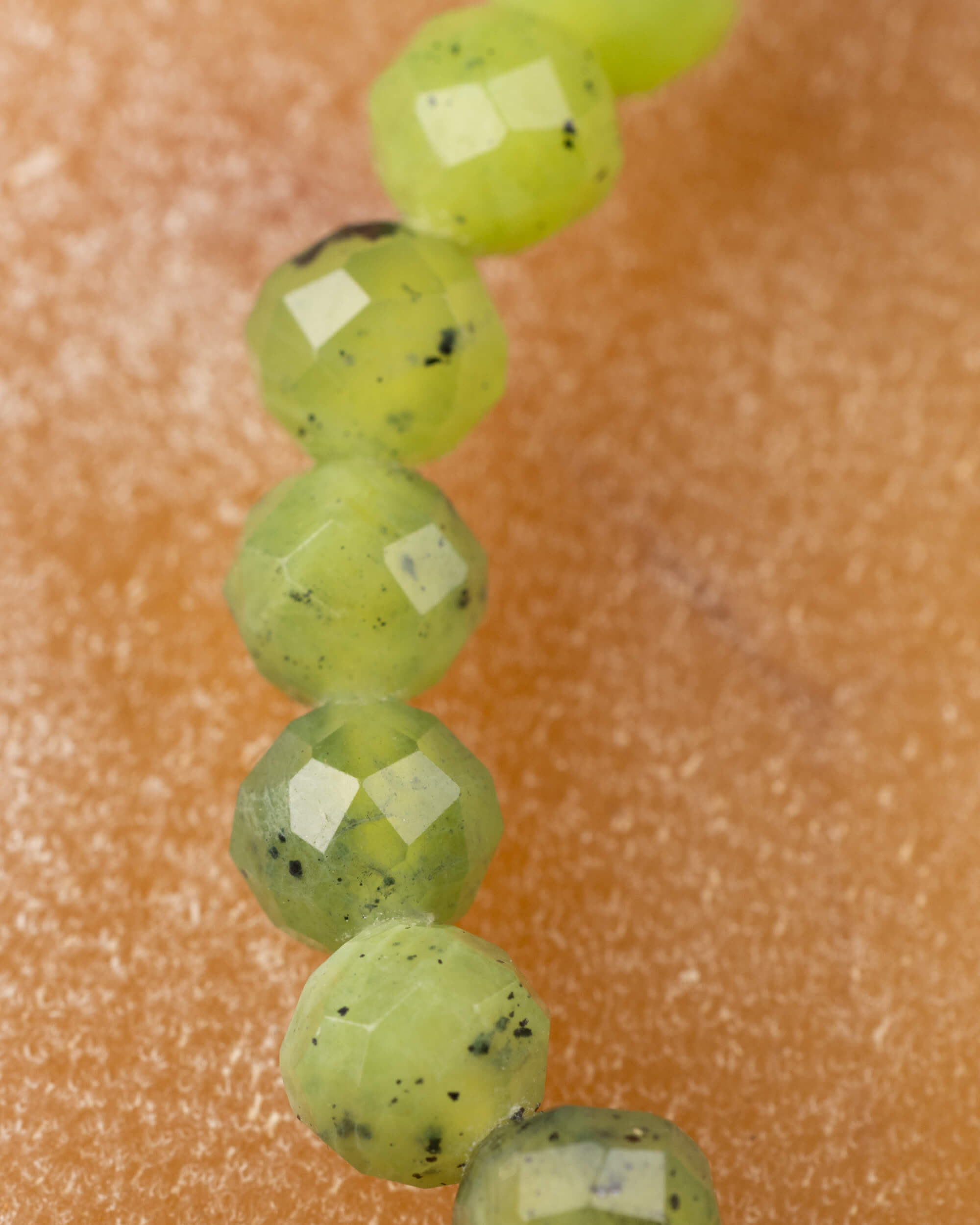 Detalle macro extremo de las cuentas facetadas de Jade Verde en fila vertical
