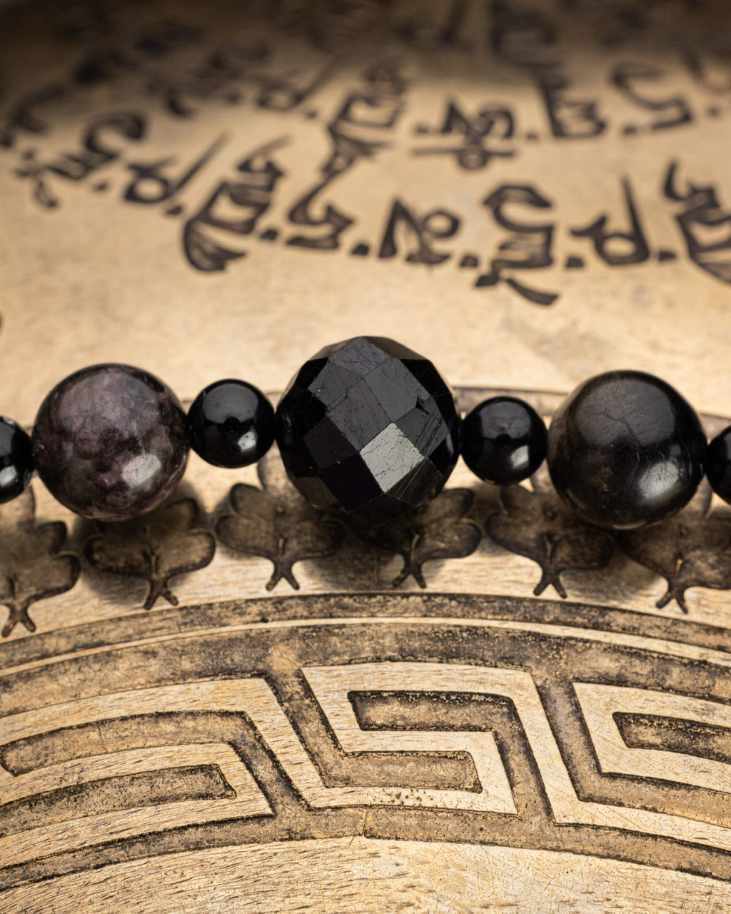Detalle macro de la cuenta facetada de Turmalina Negra entre esferas negras, con una esfera moteada rosa al borde