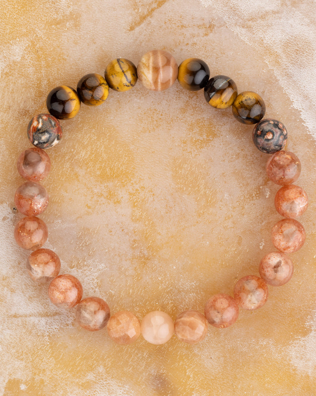 Pulsera zodiacal Leo completa, cuentas de Ojo de Tigre y piedra sol sobre superficie ocre marmoleada