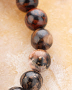 Detalle macro de las cuentas de Obsidiana Caoba en tonos rojizos y negros