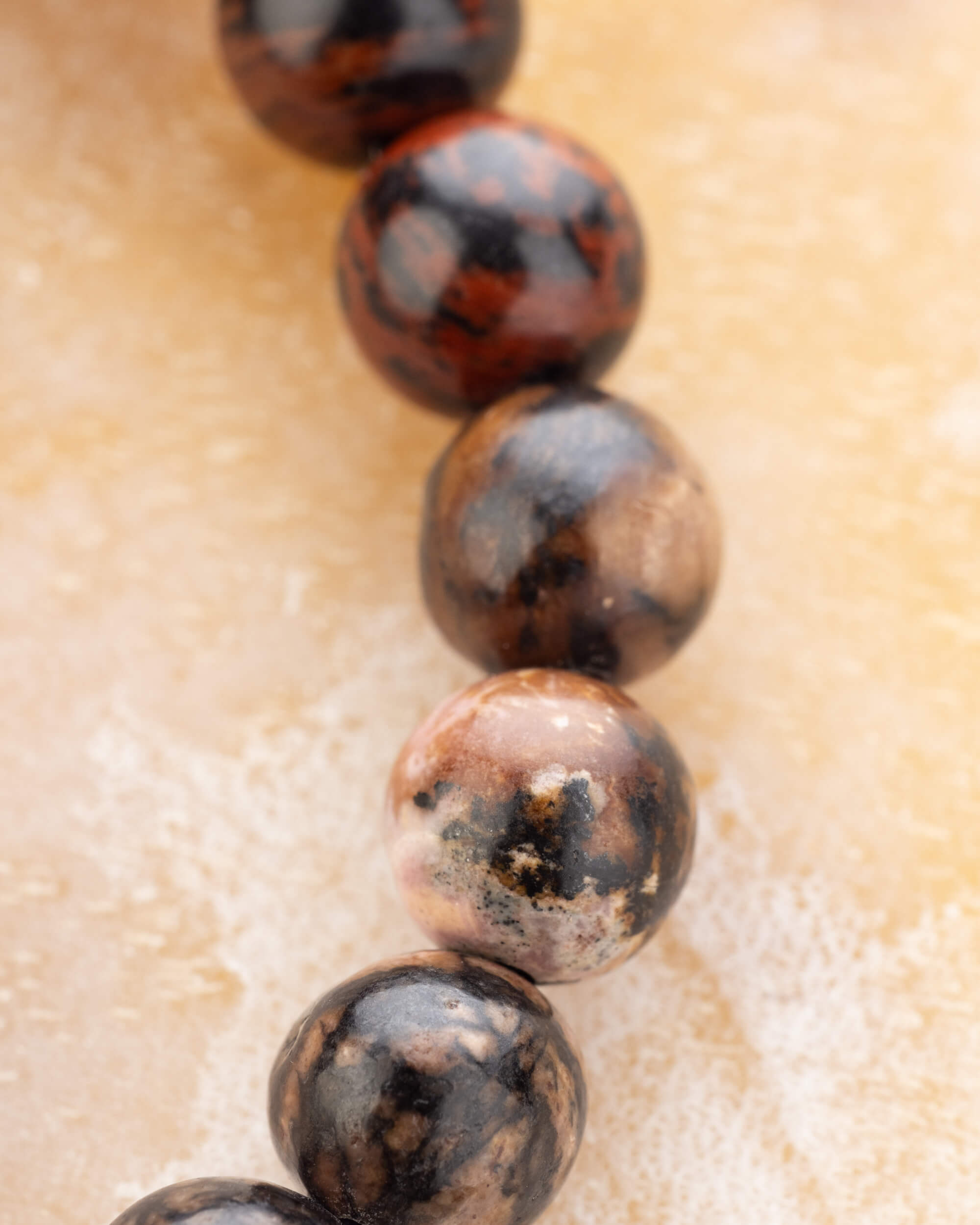Detalle macro de las cuentas de Obsidiana Caoba en tonos rojizos y negros
