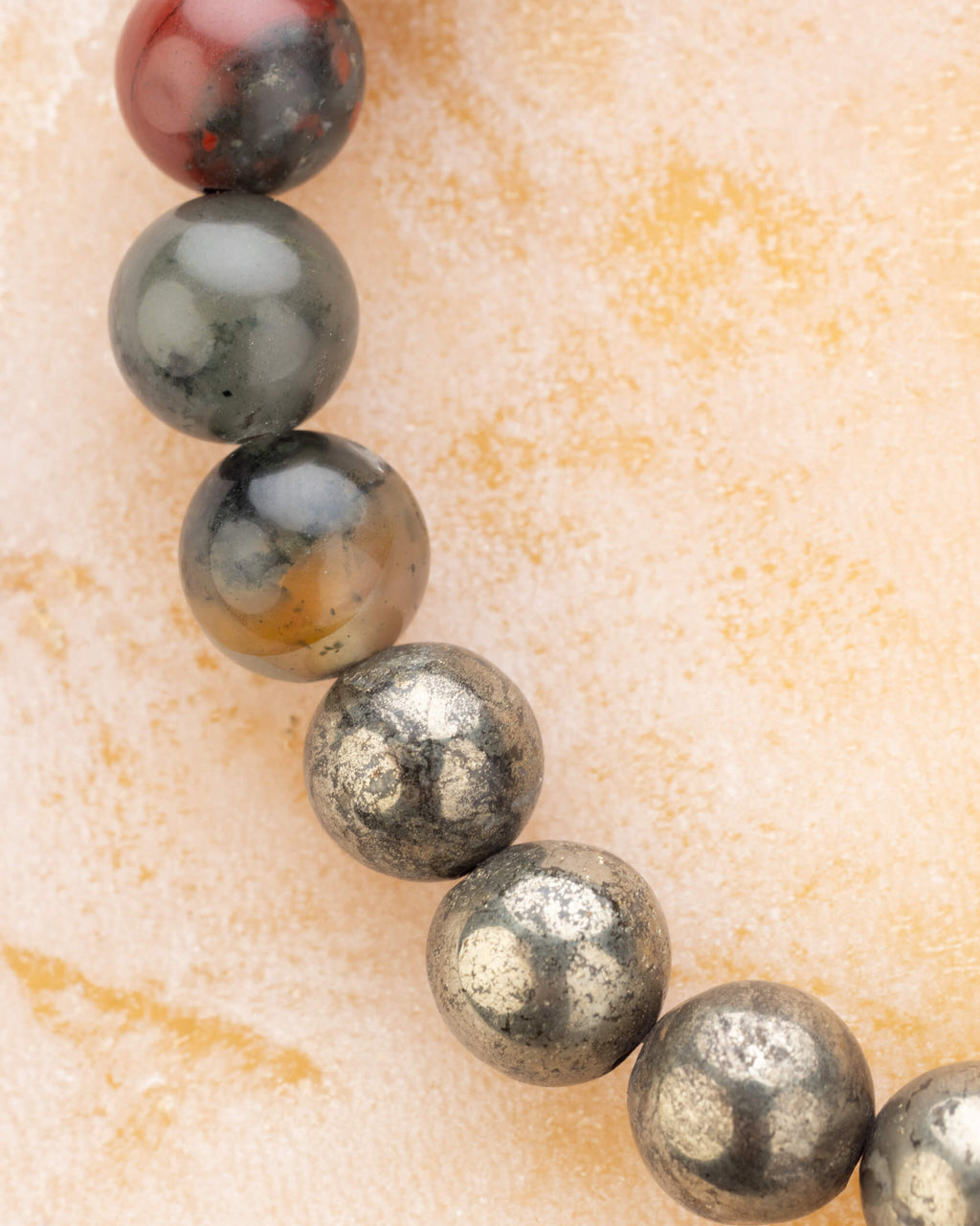 Vista en perspectiva de las cuentas de Rubí, Piedra Sangre y Pirita de la pulsera Capricornio