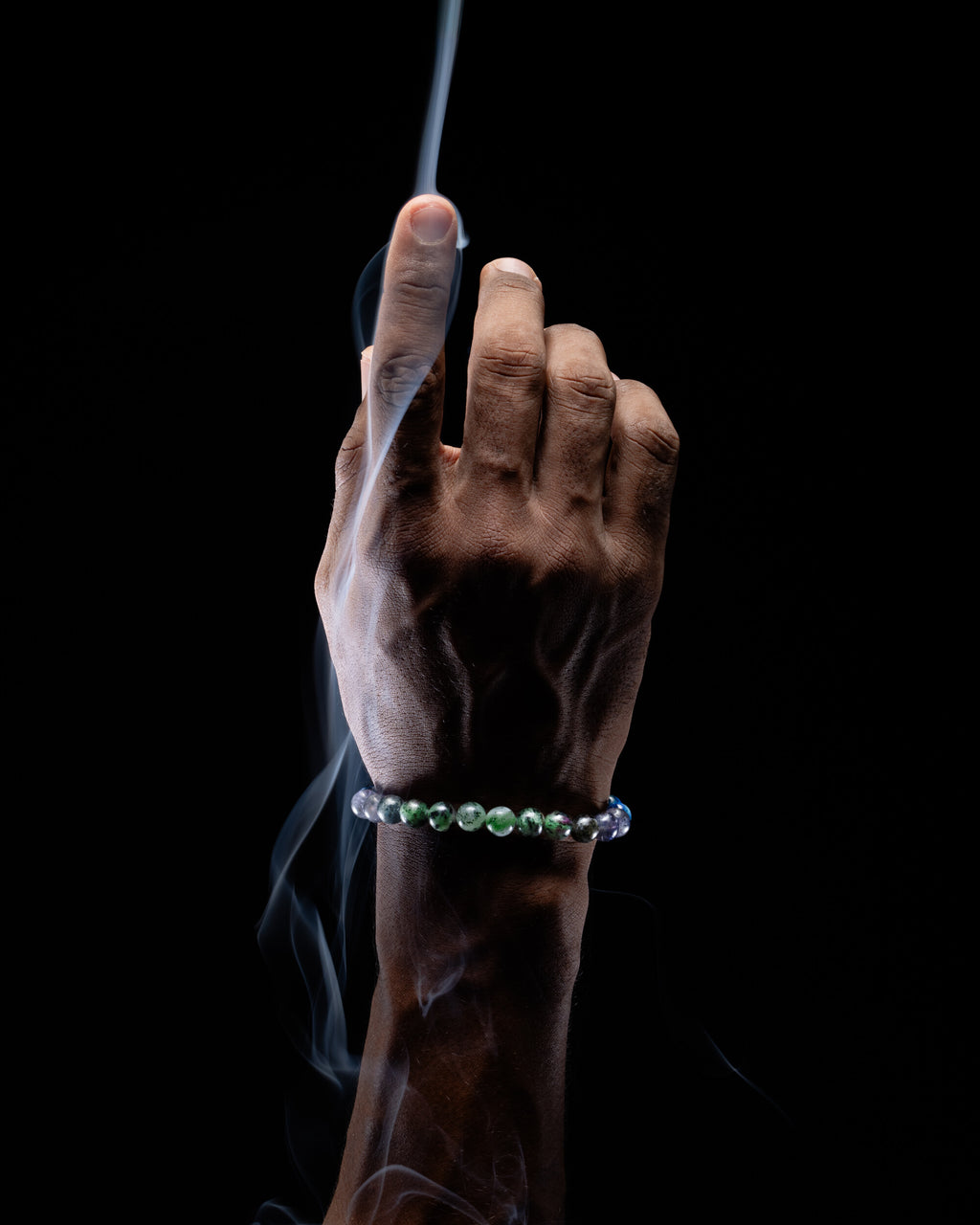 Pulsera zodiacal Libra puesta en la muñeca, dedo índice elevado entre el humo