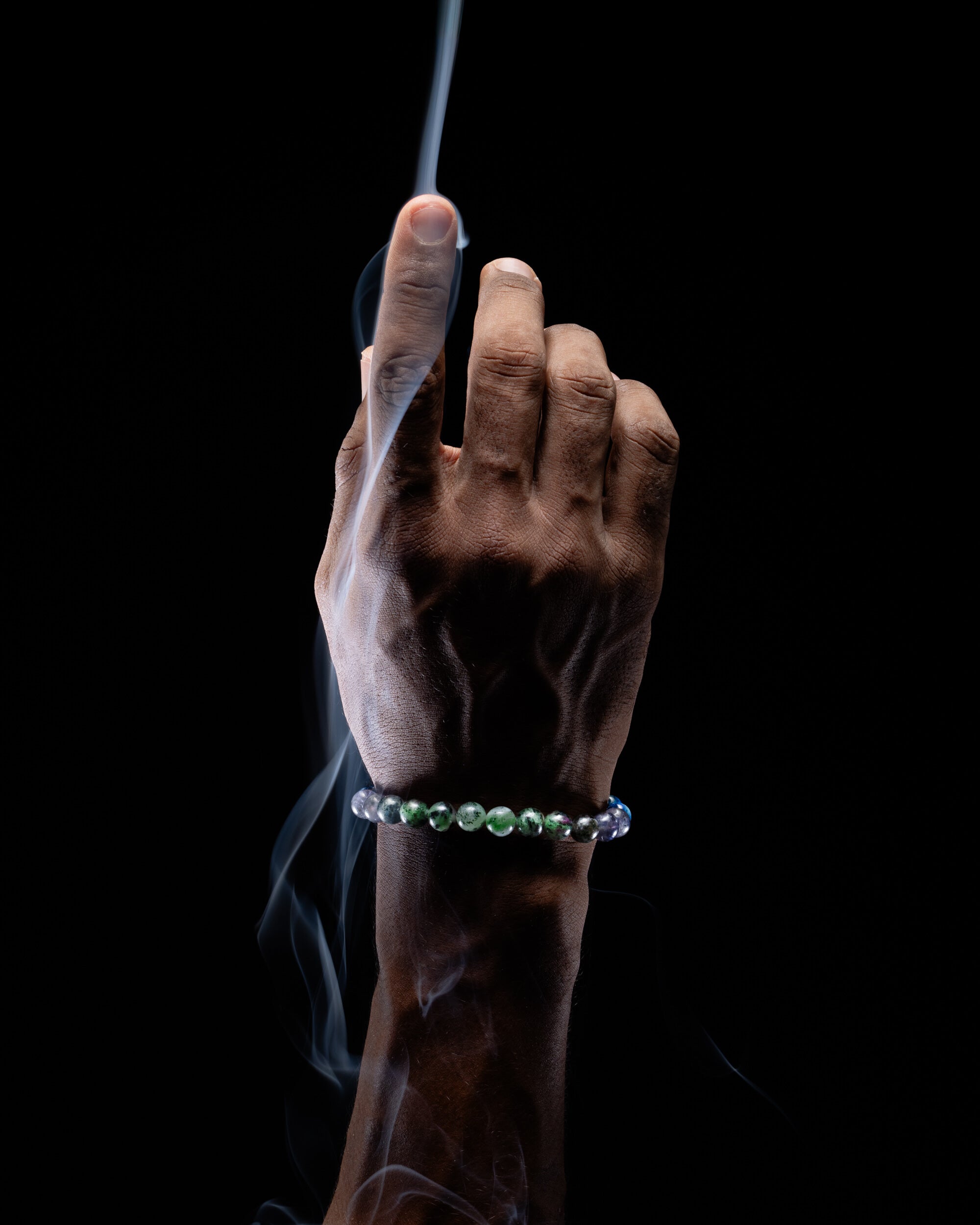 Pulsera zodiacal Libra puesta en la muñeca, dedo índice elevado entre el humo