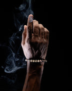 Pulsera zodiacal Sagitario puesta en la muñeca, dedo índice elevado entre el humo