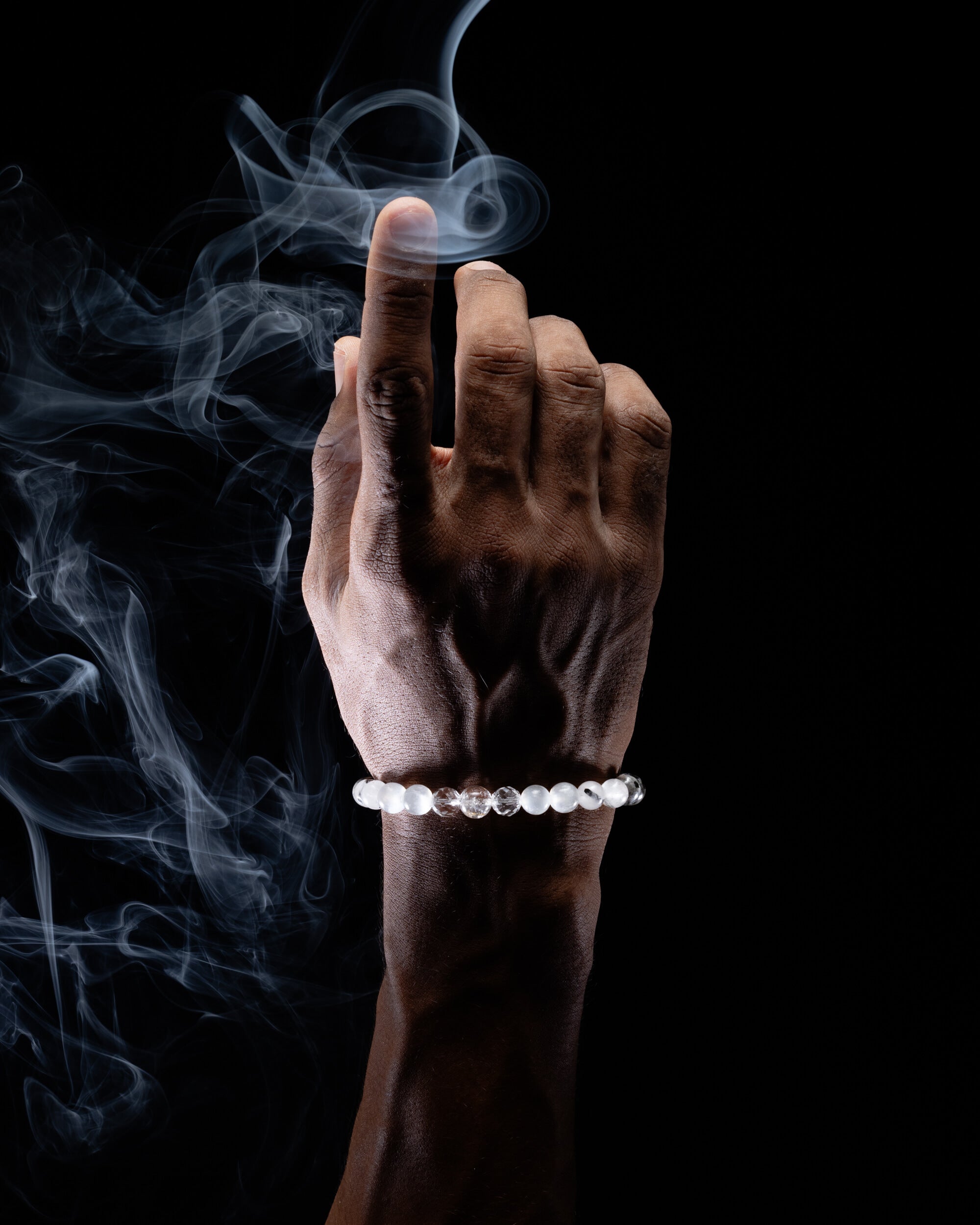 Pulsera puesta en la muñeca con esferas claras y un toque oscuro, fondo de humo