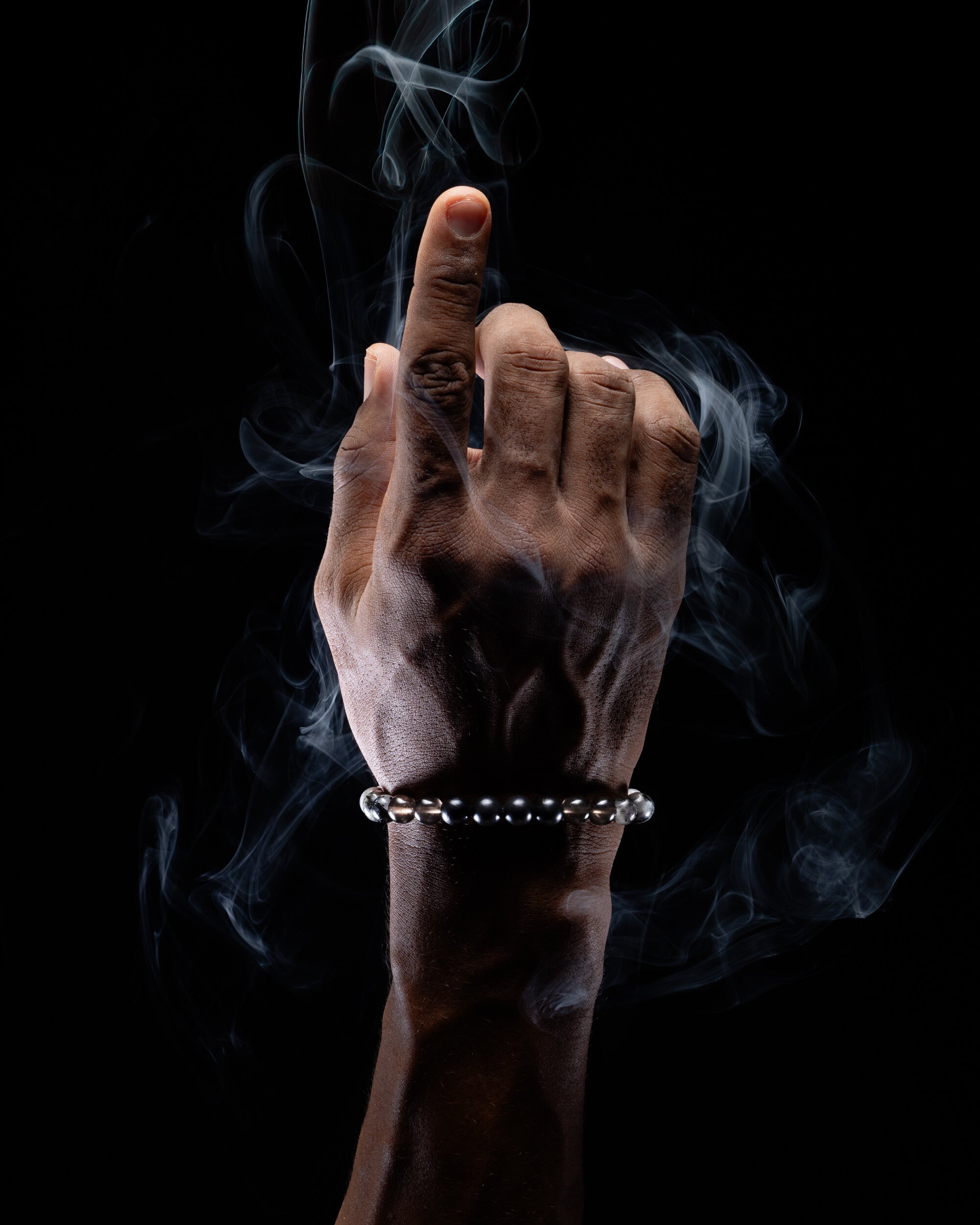 Pulsera puesta en la muñeca mostrando esferas oscuras de Larvikita, fondo de humo