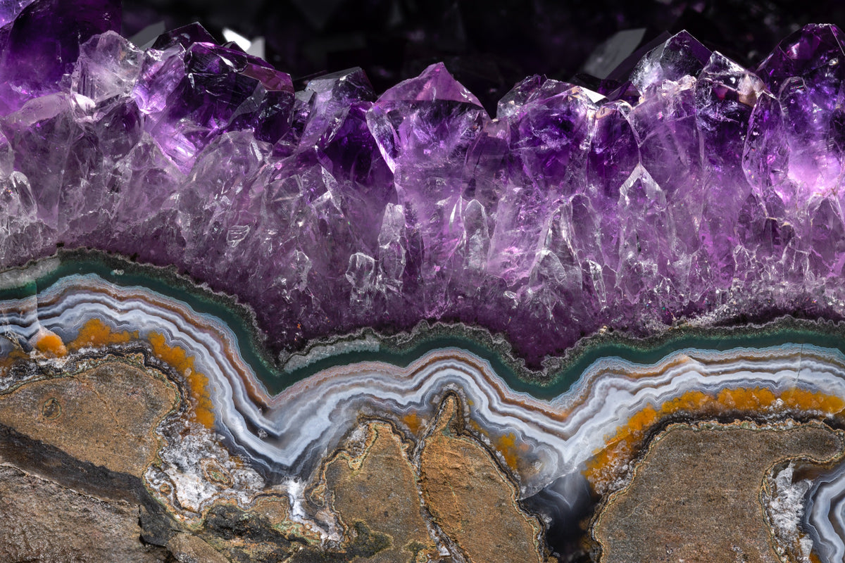 Fotografía macro de la Amatista: una fila de puntas violeta sobre bandas de ágata blanca, gris y naranja. Serie La Disolución, cuadro 10.