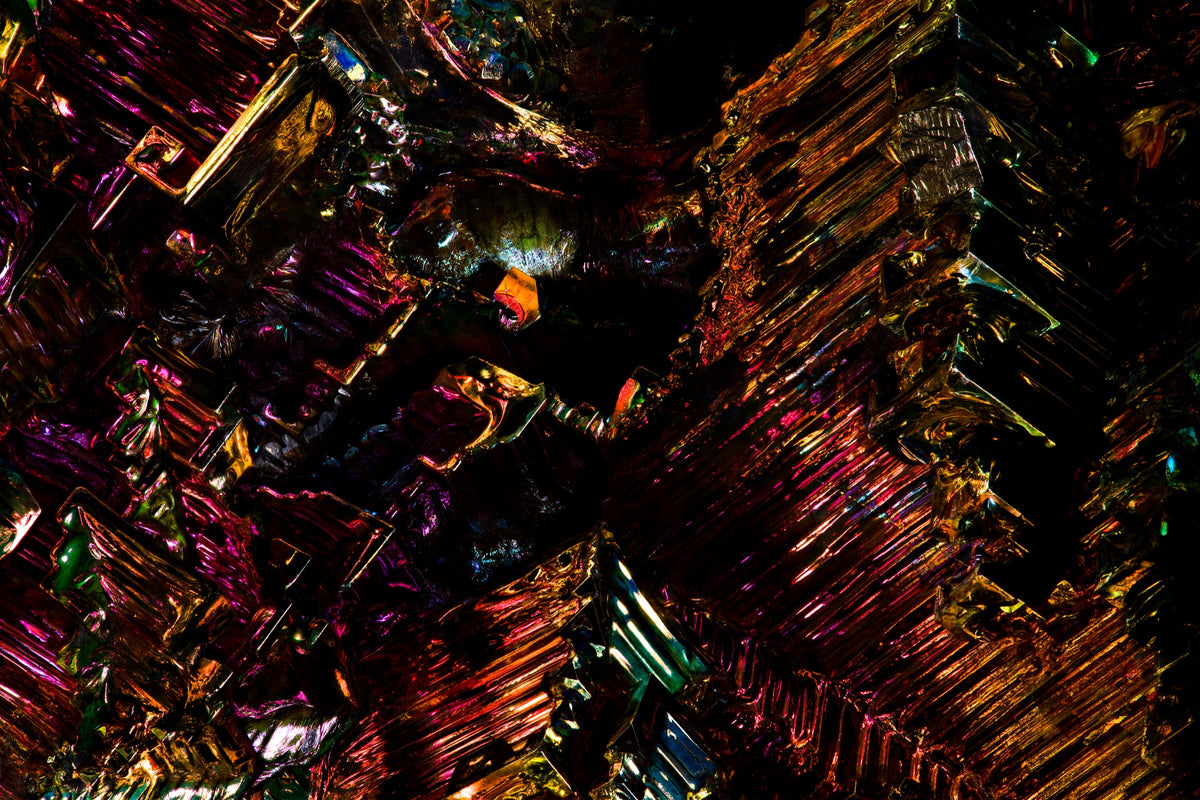 Fotografía macro del Bismuto: escaleras de cristal iridiscente en magenta, oro y verde sobre negro. Serie La Disolución, cuadro 21.