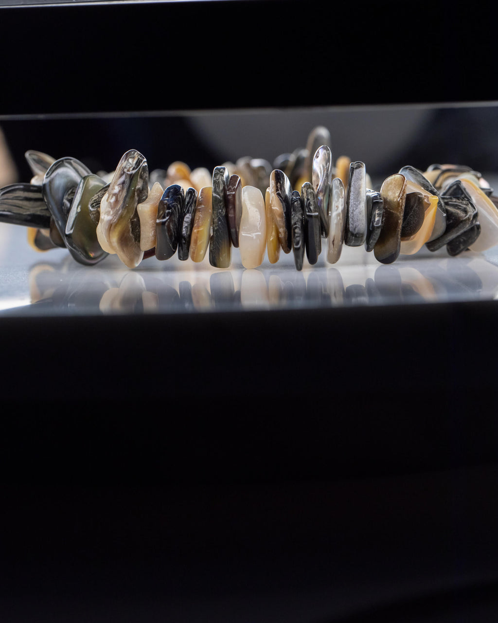 Pulsera de Abulón en fila, cuentas irregulares reflejadas sobre superficie oscura