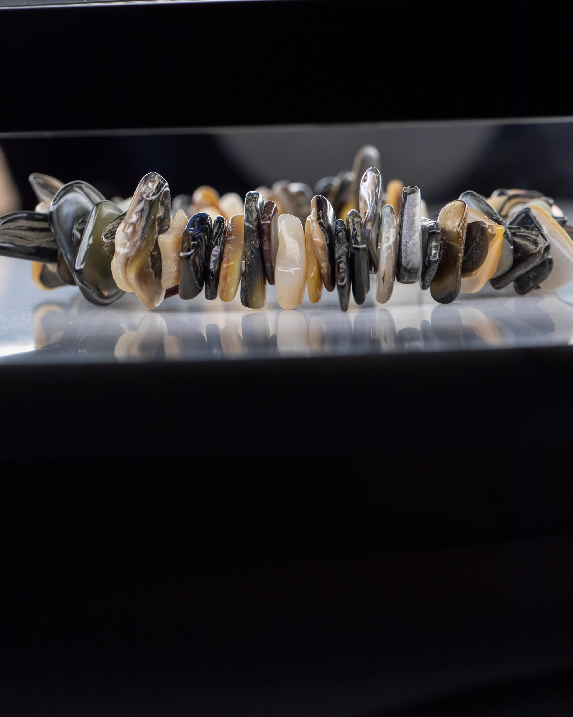 Pulsera de Abulón en fila, cuentas irregulares reflejadas sobre superficie oscura