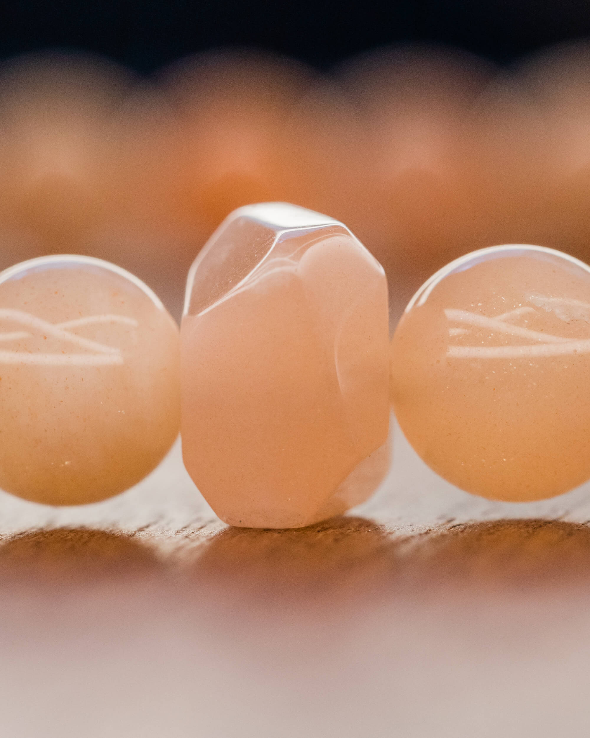 Detalle macro de una cuenta facetada de Piedra Sol Naranja entre cuentas redondas