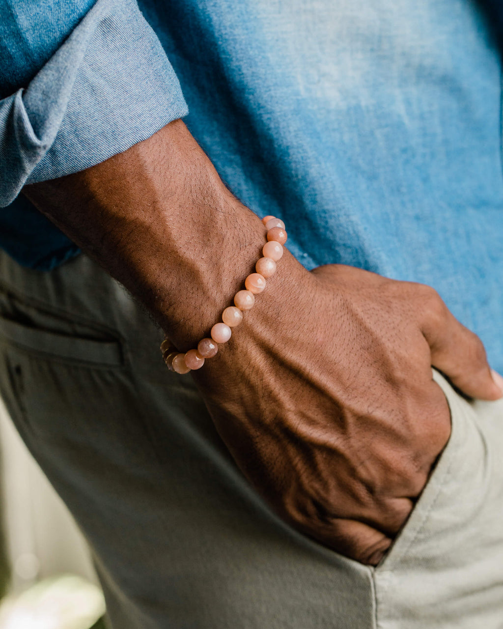 Pulsera de Piedra Sol Naranja puesta en la muñeca, con camisa azul y pantalón claro de fondo