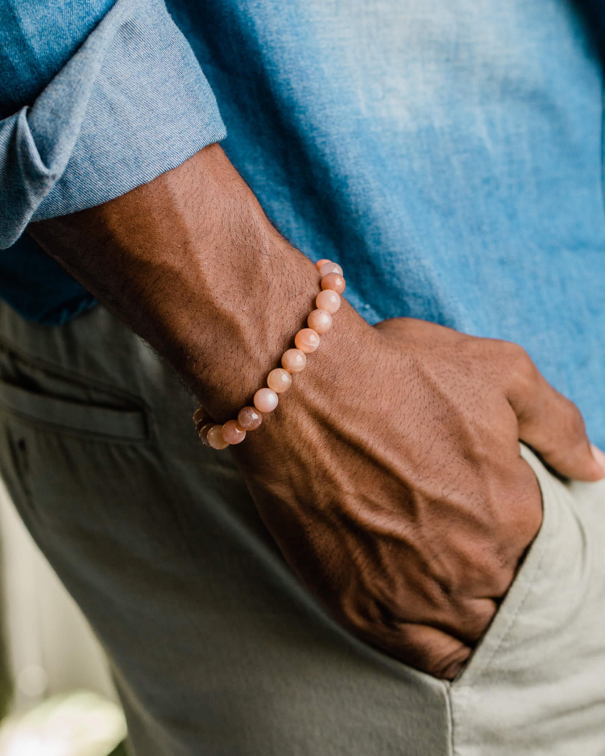 Pulsera de Piedra Sol Naranja puesta en la muñeca, con camisa azul y pantalón claro de fondo