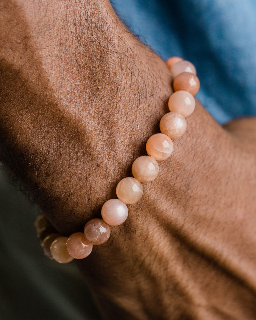 Pulsera de Piedra Sol Naranja puesta en la muñeca, con camisa azul de fondo
