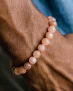 Pulsera de Piedra Sol Naranja puesta en la muñeca, con camisa azul de fondo
