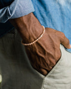 Pulsera de Piedra Sol Naranja de 4 mm puesta en la muñeca, con camisa azul de fondo