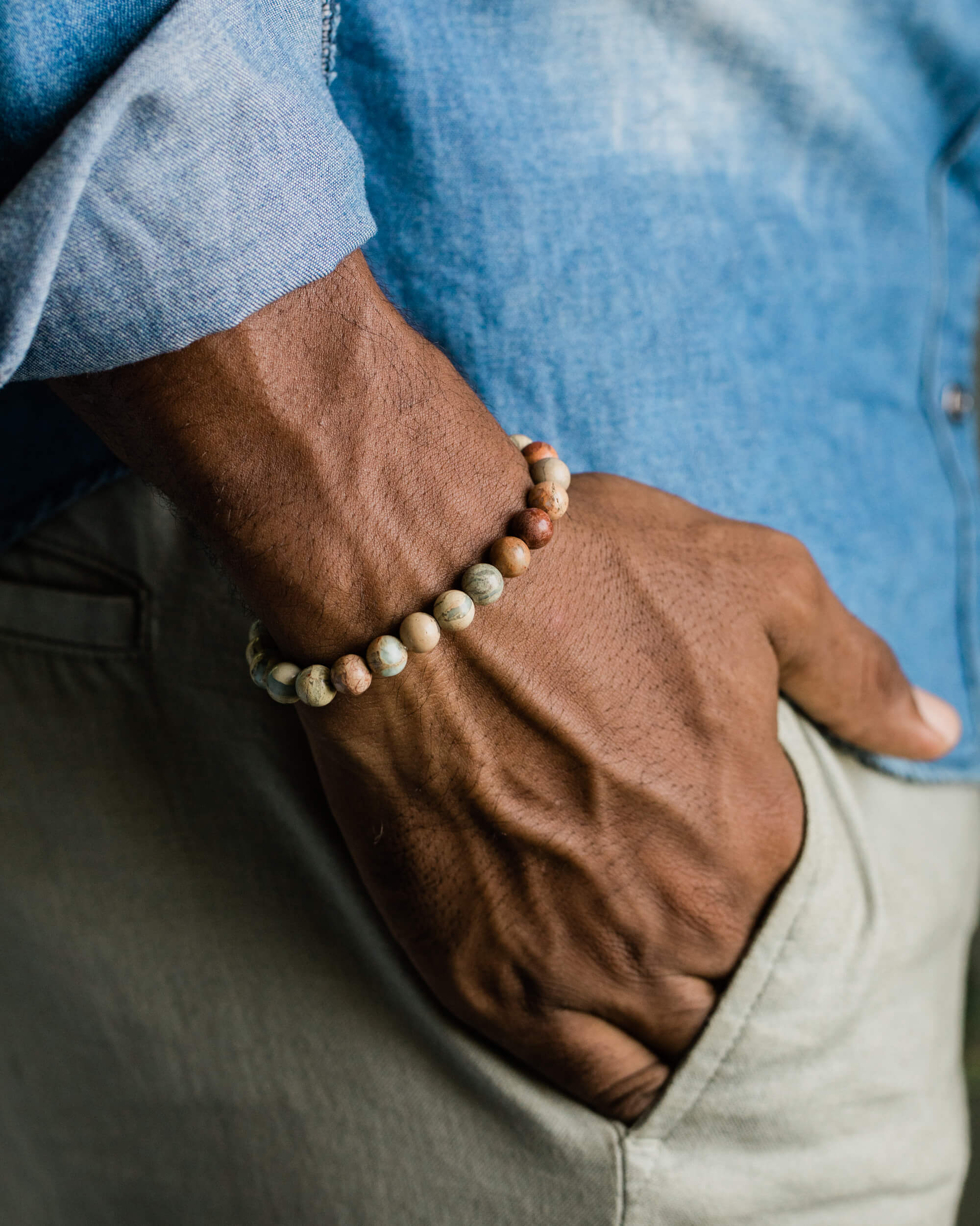 Pulsera de Shoushan puesta en la muñeca, con camisa azul y pantalón verde de fondo