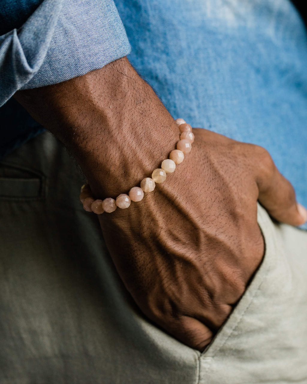 Pulsera de Piedra Sol Naranja facetada puesta en la muñeca, con camisa azul y pantalón claro de fondo