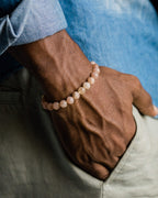 Pulsera de Piedra Sol Naranja facetada puesta en la muñeca, con camisa azul y pantalón claro de fondo