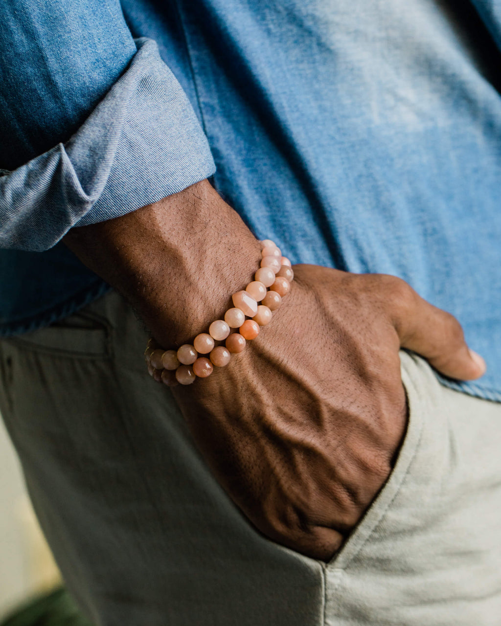 Codificador de Piedra Sol Naranja puesto en la muñeca junto a otra pulsera, mano en el bolsillo