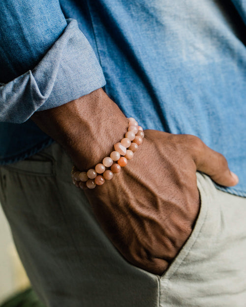 Codificador de Piedra Sol Naranja puesto en la muñeca junto a otra pulsera, mano en el bolsillo
